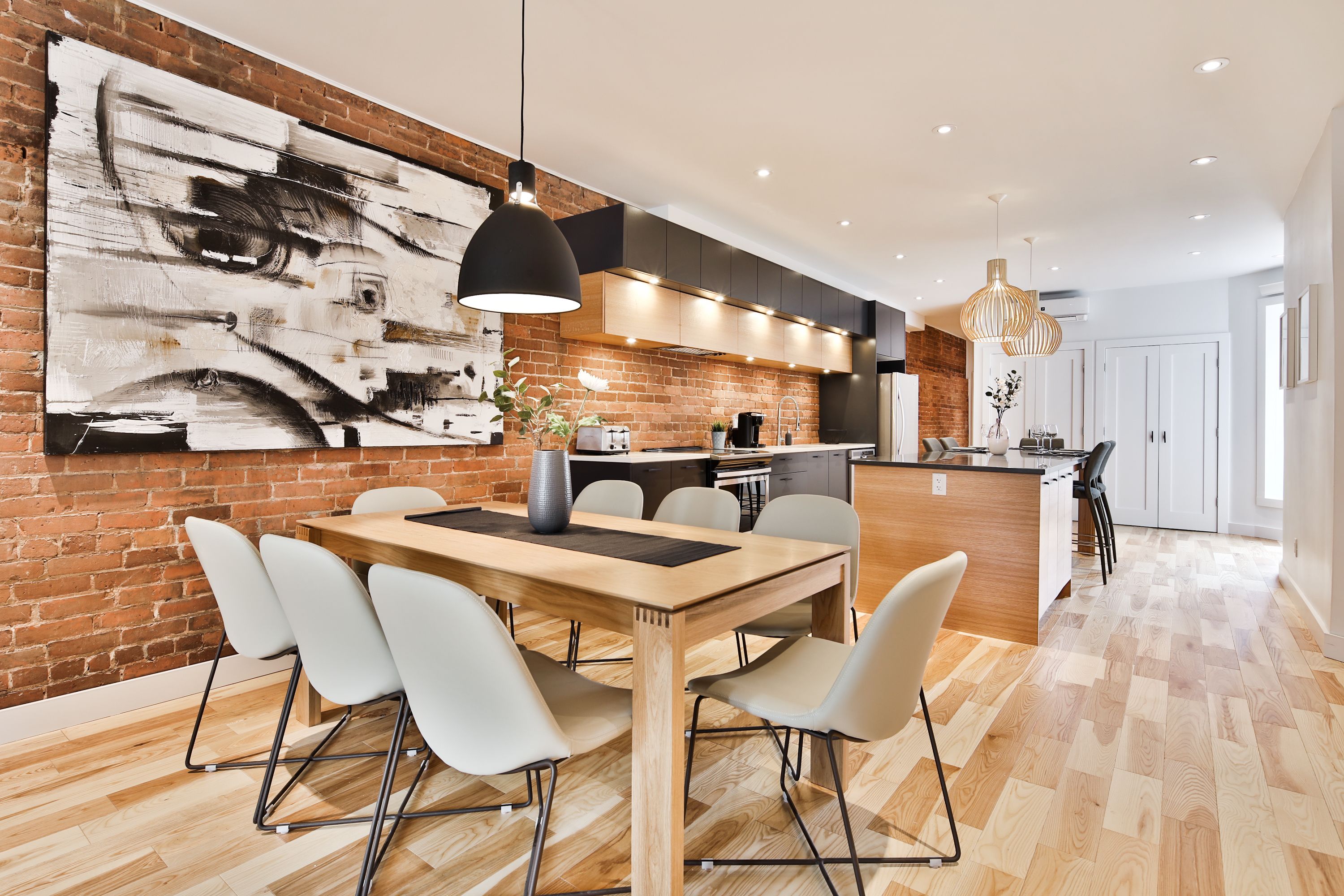 A modern kitchen with a large abstract painting, a wooden dining table with chairs, and a kitchen island.