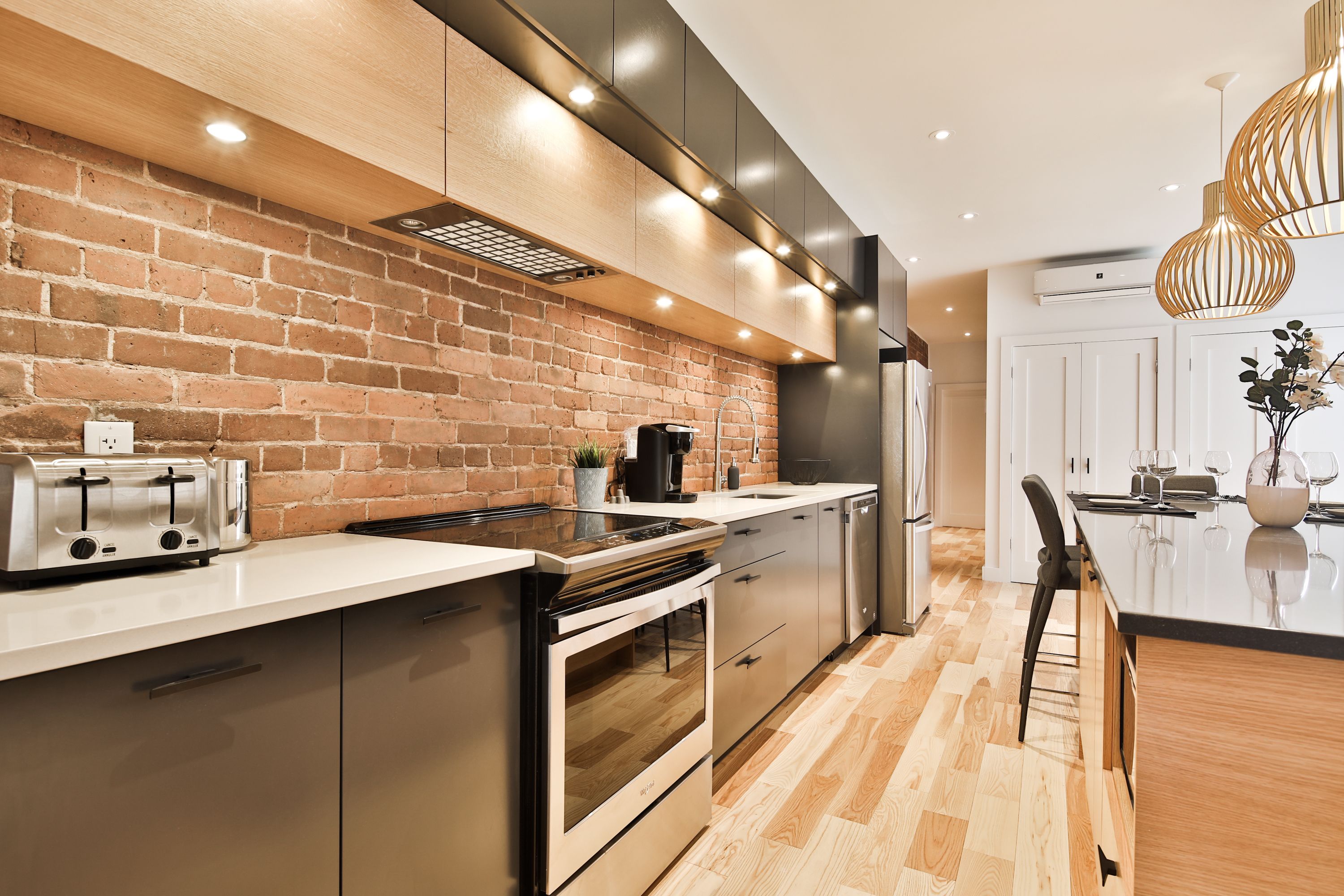 A modern kitchen with a brick wall, stainless steel appliances, and a wooden floor.