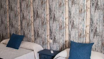 Two single beds with blue pillows, a small bedside table, and a wall with a rustic wooden texture.