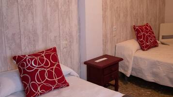 A hotel room with two beds, each with a red pillow, a small wooden nightstand, and a white wall.