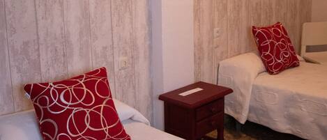 A hotel room with two beds, each with a red pillow, a small wooden nightstand, and a white wall.