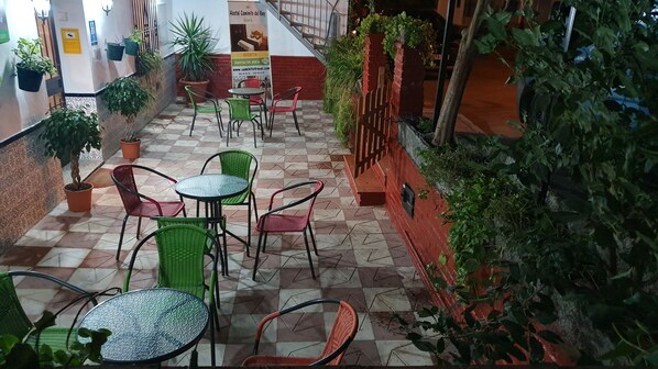 A courtyard with tiled flooring, green and red wicker chairs, and potted plants.