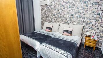 Un dormitorio con pared de diseño de piedra, una cama con ropa de cama estampada, una mesita de noche de madera y una lámpara de mesa pequeña.
