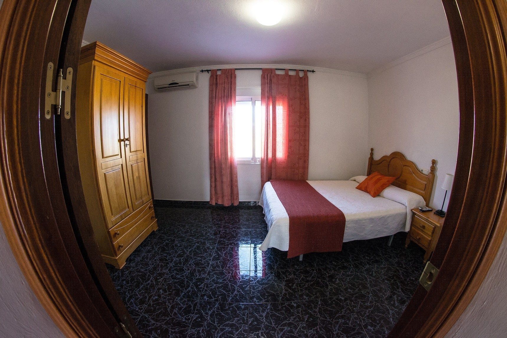 A bedroom with a bed, a wooden wardrobe, a nightstand, and a window with curtains.