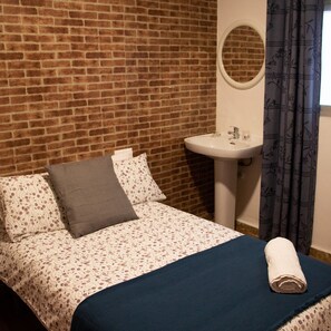 A room with a brick wall, a bed with floral bedding, a white sink, and a blue curtain.
