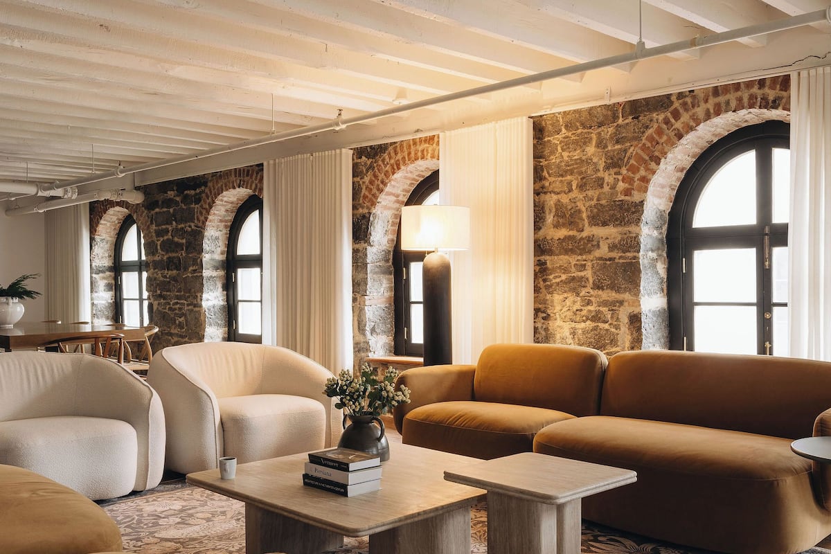 A cozy living room with a stone wall, arched windows, and a mix of modern and classic furniture.