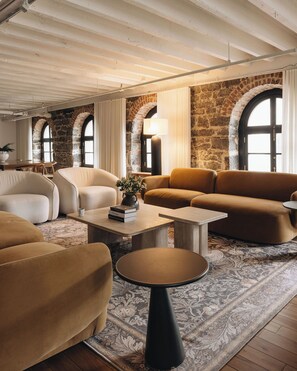 Ein gemütliches Wohnzimmer mit Steinwand, Rundbogenfenstern und einer Mischung aus moderner und klassischer Möbel.