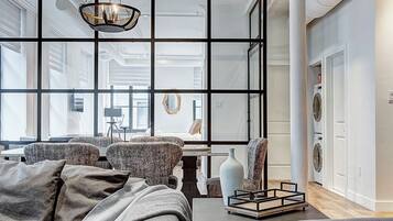 A modern bedroom with a large bed, a seating area with a chair, a hanging light fixture, and a view through a glass partition.