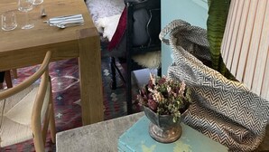 Un comedor con una mesa de madera dispuesta para una comida, un sofá con cojines estampados y un cuadro de paisaje enmarcado en la pared.