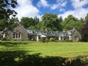 A stone building with multiple chimneys, a lawn, and a picnic table. - The Cnoc Hotel (Beauly)