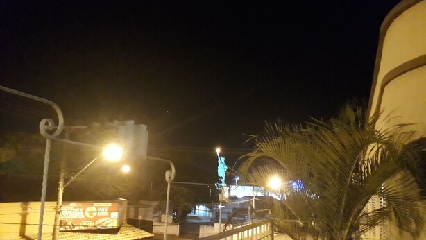 Une vue nocturne d’une rue avec une statue, des lampadaires et un palmier.