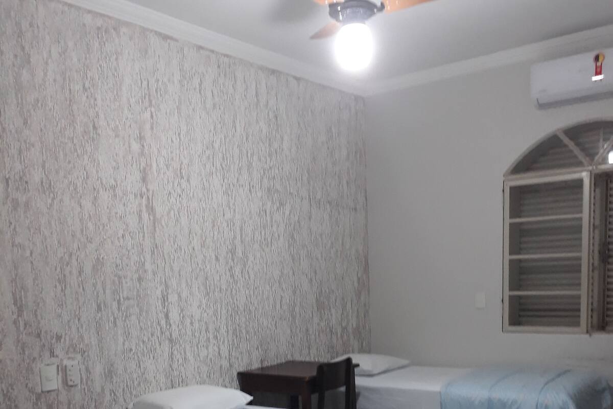 Habitación con tres camas, ventilador de techo y ventana con persianas.