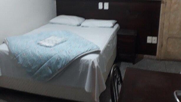 A bedroom with a bed, a nightstand, a wooden table, and a wall-mounted artwork. - Araça Hotel (Aracatuba)