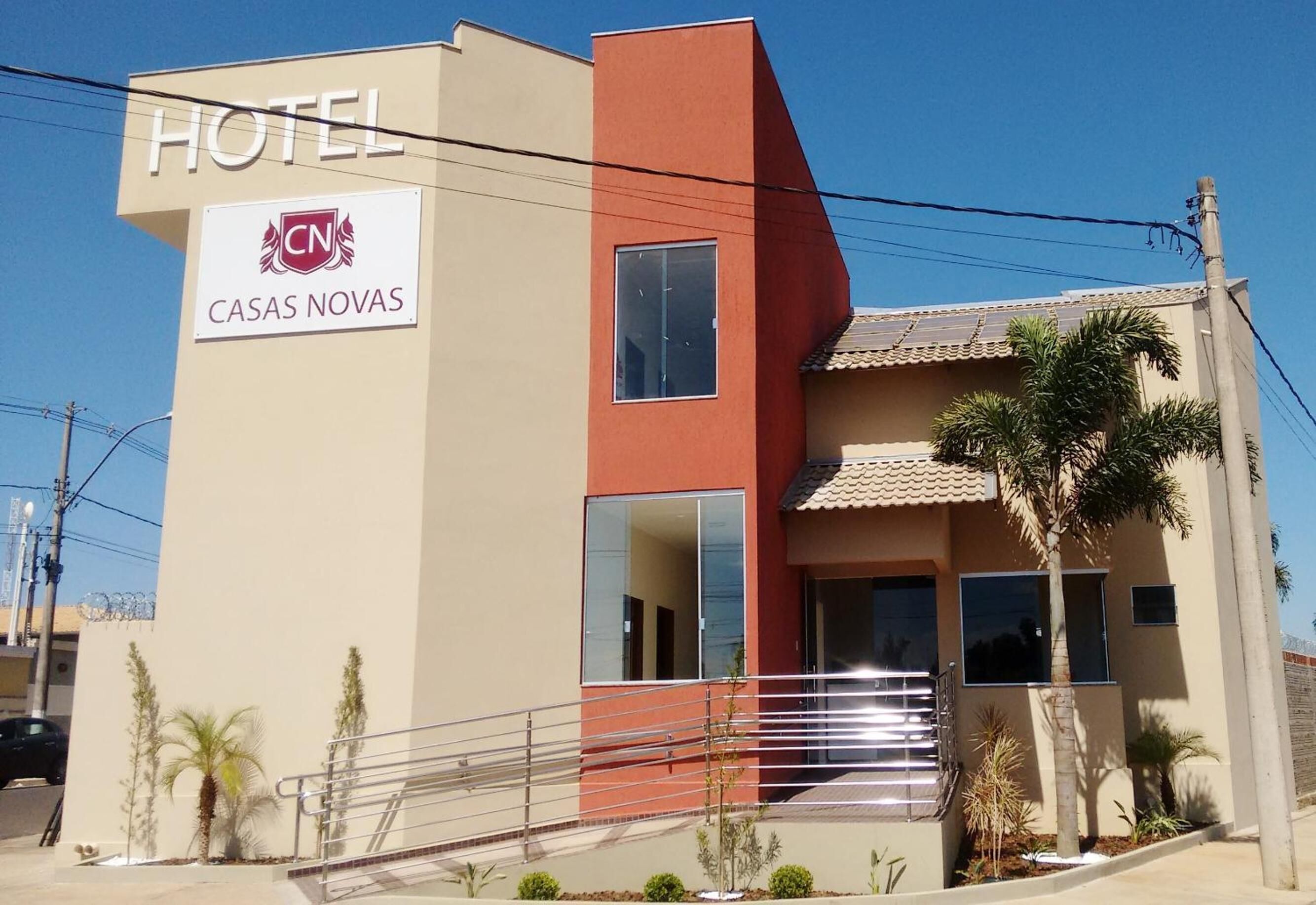 Um hotel chamado 'CASAS NOVAS' com design moderno, apresentando uma placa chamativa com a palavra 'HOTEL', uma parede de destaque vermelha e um telhado telhado.