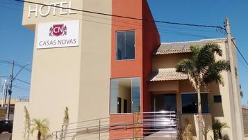Um hotel chamado 'CASAS NOVAS' com design moderno, apresentando uma placa chamativa com a palavra 'HOTEL', uma parede de destaque vermelha e um telhado telhado.