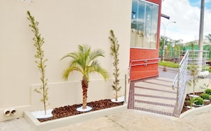 A building with a red exterior, a palm tree, and a staircase leading to a balcony. - Hotel Casas Novas (Penapolis)