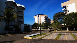 A residential building with multiple balconies, a paved courtyard, and surrounding greenery. - Enseada Nautico - JC Temporada (Caldas Novas)