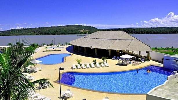 A resort with a large swimming pool, lounge chairs, and a view of a lake. - Enseada Nautico - JC Temporada (Caldas Novas)