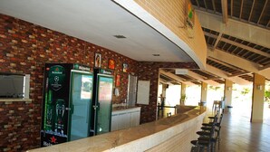 A bar area with a brick wall, two refrigerators, and a long counter with bar stools. - Enseada Nautico - JC Temporada (Caldas Novas)