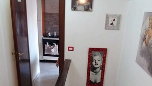 A staircase with a handrail, a wall with a framed picture, and a door leading to a room with a kitchen area. - M & I Apartment (Fiumicino)