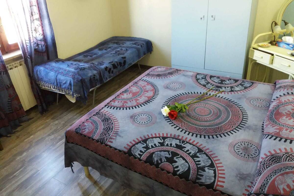 A room with a bed, a bench, a wardrobe, and a desk with a lamp.