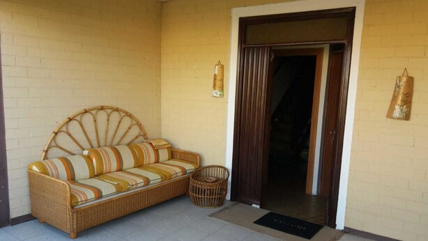 A wicker sofa with striped cushions, a wicker chair, and a door leading to an interior space. - M & I Apartment (Fiumicino)