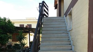 A set of concrete stairs leading up to a building with a yellow door and a black handrail. - M & I Apartment (Fiumicino)