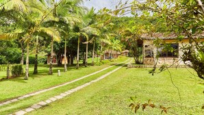 A pathway leading to a row of traditional-style buildings surrounded by lush greenery and palm trees. - Pousada Villa da Glória (São Francisco do Sul)