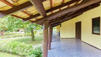 A covered outdoor area with a tiled floor, wooden beams, and a yellow wall with a window and door.