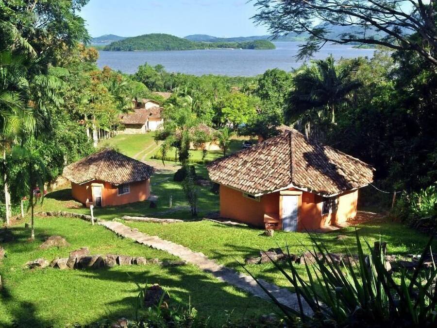 Un resort tropical con cabañas de techo de paja, exuberante follaje y vista a un lago.