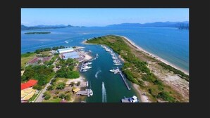 An aerial view of a coastal marina with boats docked along the shore, a pier extending into the water, and a building complex with a red roof. - Pousada Villa da Glória (São Francisco do Sul)
