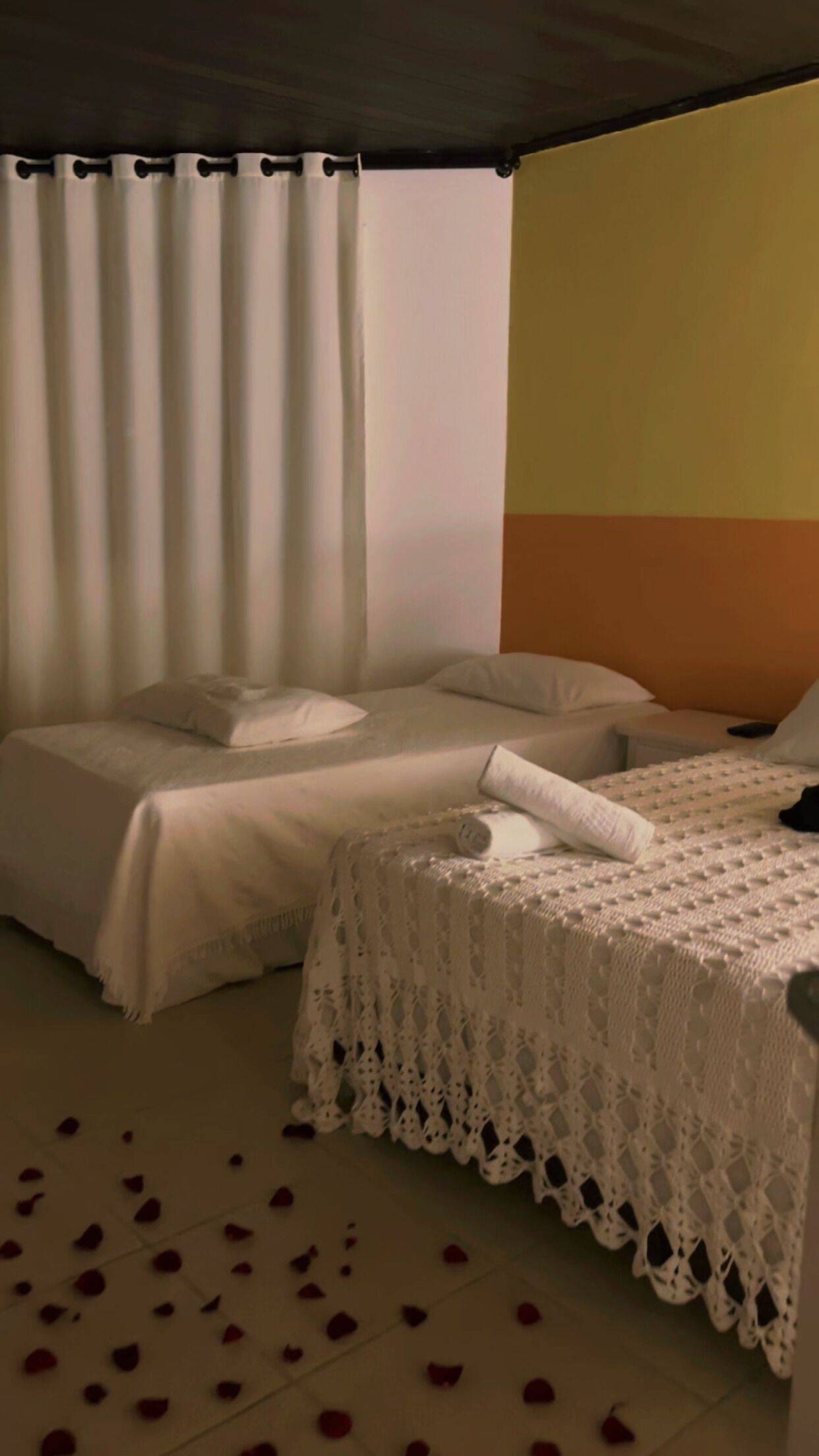A room with two beds, each covered with white linens and a lace bedspread.