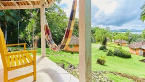 A hammock on a porch with a bench, surrounded by a lush garden and a view of houses in the distance. - Pousada Villa da Glória (São Francisco do Sul)