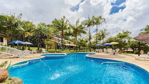 A large, clear swimming pool surrounded by palm trees and lounge chairs. - Pousada Villa da Glória (São Francisco do Sul)