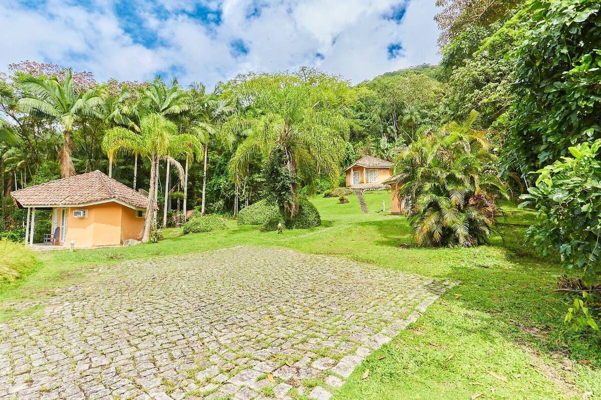 Uma casa rústica com telhado de cerâmica, rodeada por vegetação exuberante e palmeiras.