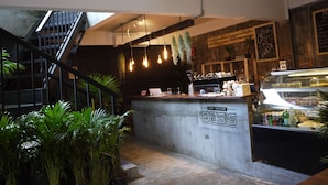 Ett kafé med en bardisk i betong, hängande lampor och en trappa.