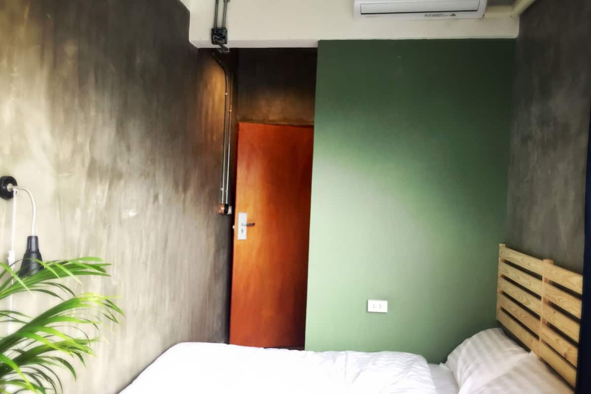 Ein Schlafzimmer mit einem Bett, einem hölzernen Kopfteil, einer grünen Wand, einer Holztür und einer Pflanze.