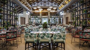 A spacious dining area with multiple tables and chairs, high ceilings with exposed beams, and numerous potted plants. - Be Live Collection Punta Cana - Adults Only (Punta Cana)