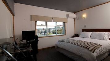 Una habitación de hotel con una cama, un escritorio con ordenador, una silla, un ventanal con vistas a la ciudad y un equipo de aire acondicionado.
