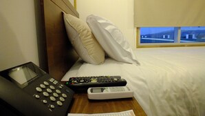 A hotel room with a bed, pillows, a bedside table with a telephone, a remote control, and a digital clock. - Hotel Terrapuerto (Valdivia)