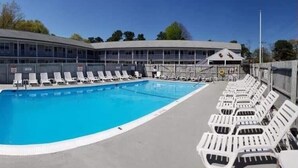 A swimming pool with lounge chairs and a building with a curved roof. - Doryman Motel (Dennis Port)