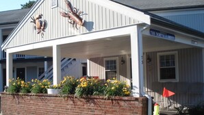 A motel with a covered porch, a brick wall, and yellow flowers. - Doryman Motel (Dennis Port)
