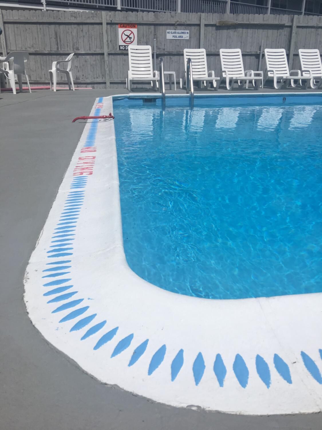 Una piscina con agua azul, borde blanco y un cartel que indica prohibido llevar vidrio.