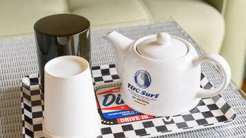A table with a white teapot, a white cup, and a black container on a checkered placemat.