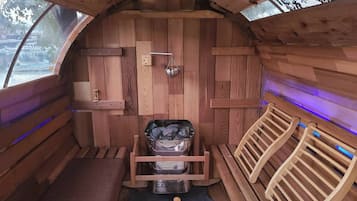 Una cabaña de madera con sauna integrada, bancos de madera y un contenedor metálico.