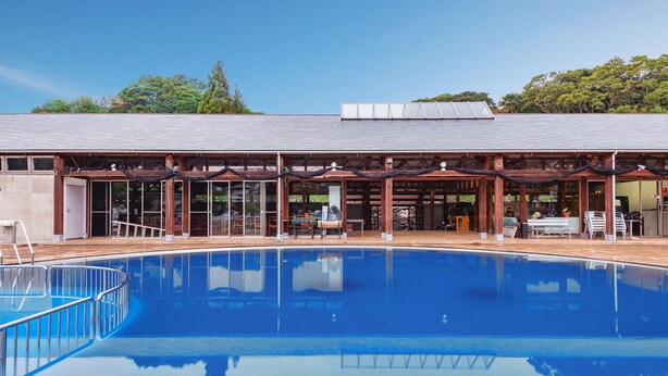A swimming pool with a wooden deck and glass doors, surrounded by a covered area with tables and chairs. - Tabist Villa Daioh Resort Iseshima (Shima)