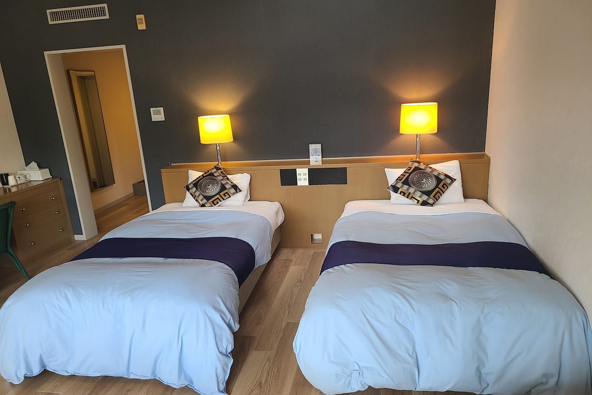 A hotel room with two beds, each with a headboard, bedside lamps, and decorative pillows.