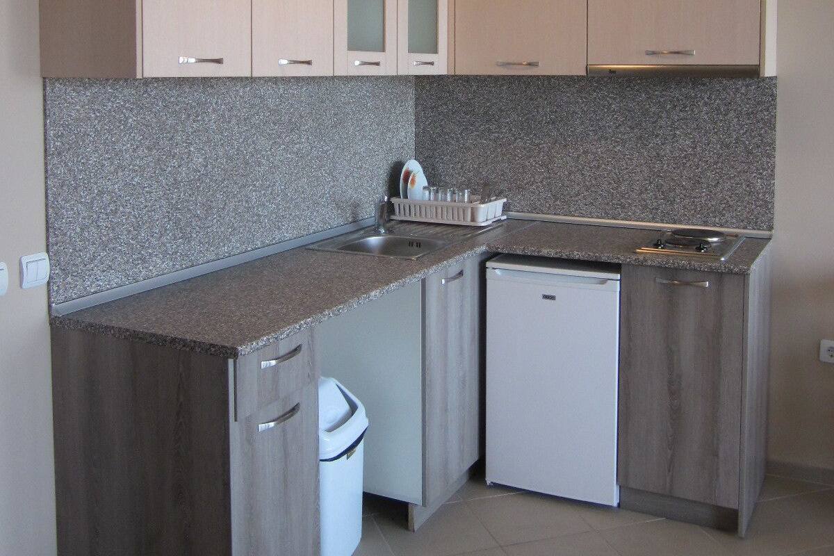A compact kitchen with granite countertops, white cabinetry, and a built-in dishwasher.