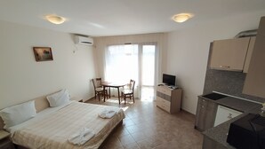 A hotel room with a bed, a desk, a chair, a television, a kitchen area, and a window with curtains. - Sunny Sands Studios (Burgas)