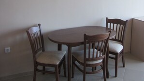 A dining area with a round table and four wooden chairs, a painting on the wall, and a tiled floor. - Sunny Sands Studios (Burgas)